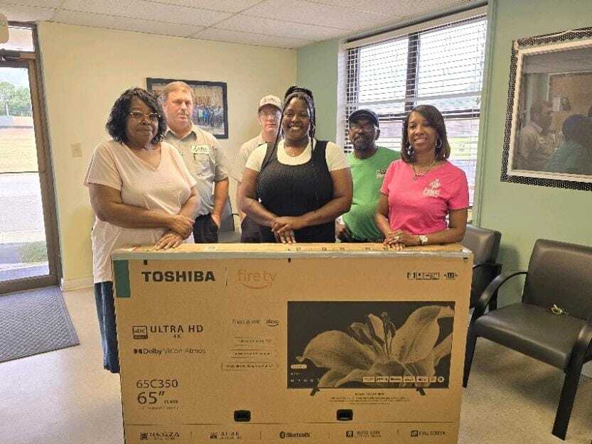 Janeva McCullen winner of a brand new 65 inch tv with Fairview Staff posing for a group shot inside office